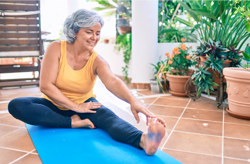a woman in a yellow shirt is sitting and reaching for her right foot on a yoga mat