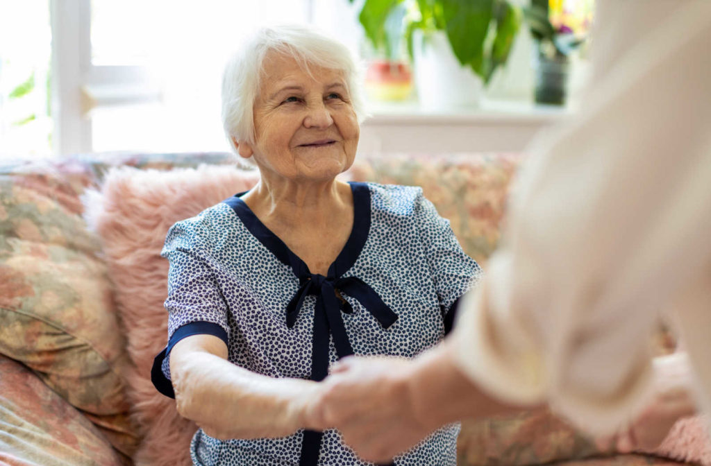 An older woman with dementia holding hands and smiling at someone else