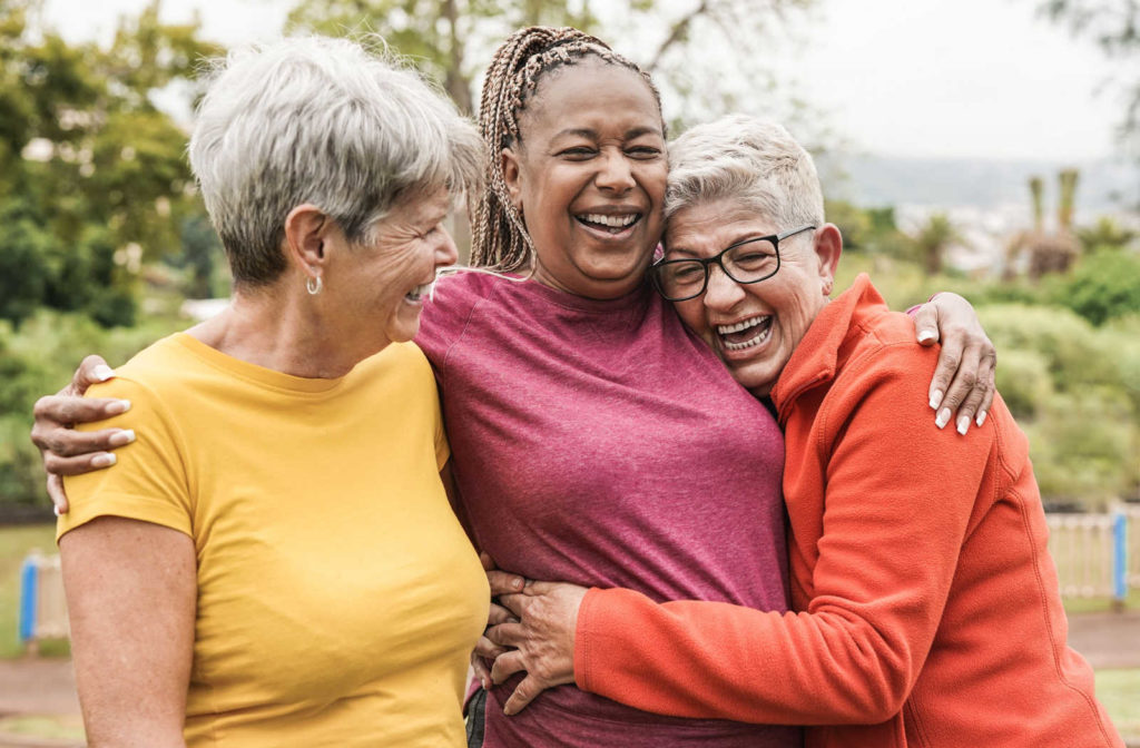 A group of three senior women hugging and laughing while out for a walk.