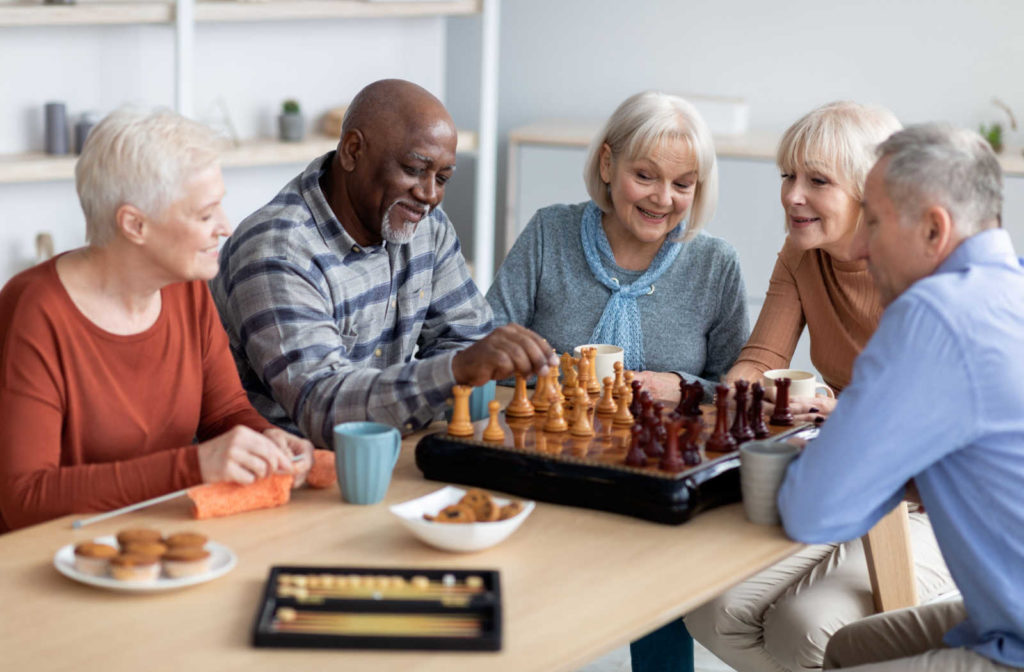 A group of seniors hanging out and playing chess while enjoying some snacks.
