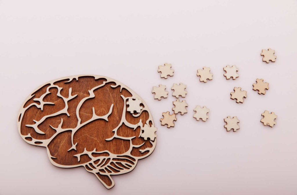 Image of a brain cut out from wood, with puzzle pieces laid around it.
