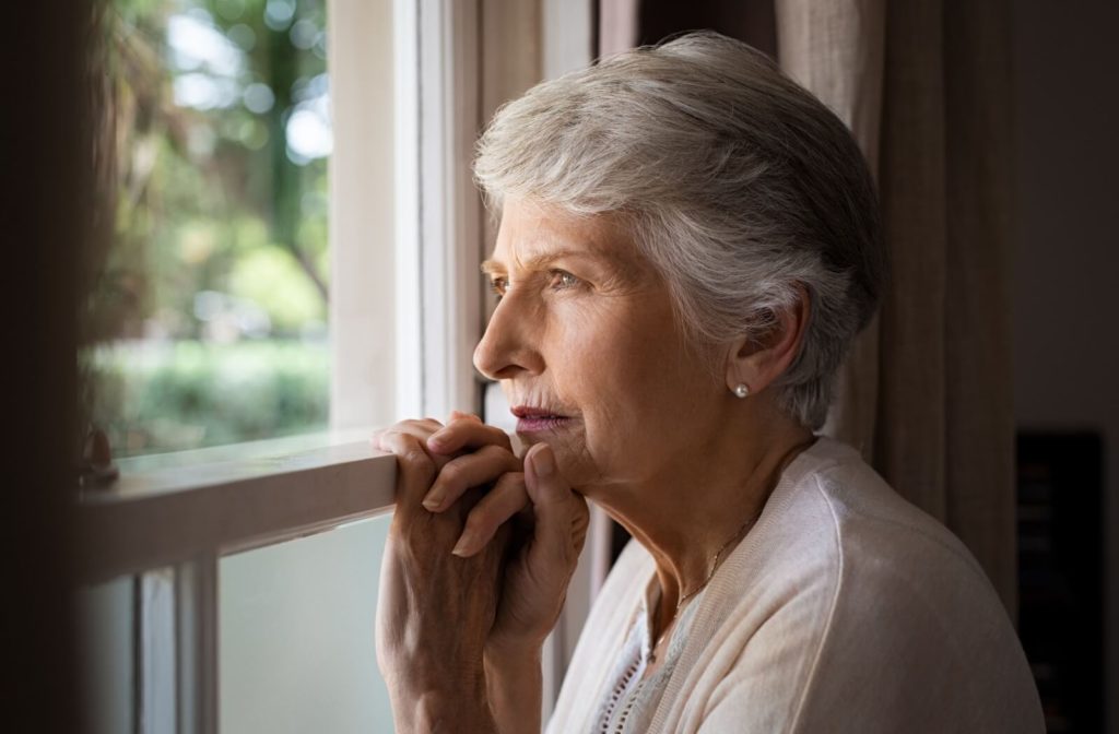 An older adult with memory loss looks solemnly out a window.