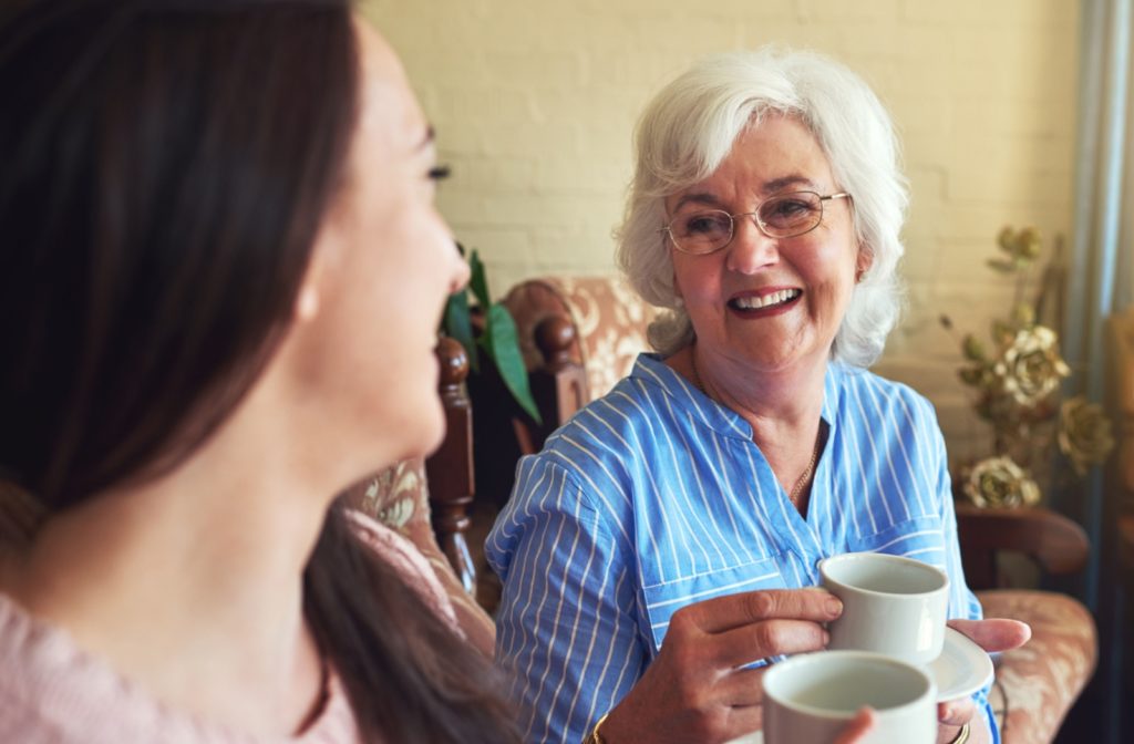 A senior with dementia smiles at their adult child who has come to visit them for tea and chat.