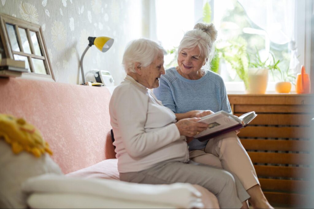 An adult smiles while looking through a photo album with their older parent with dementia after settling into memory care