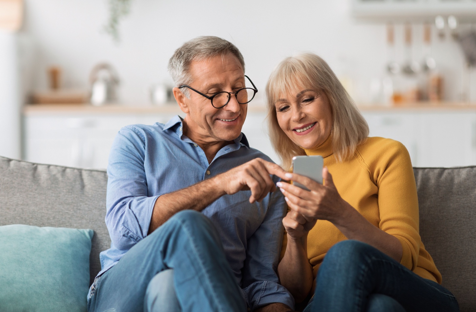 An older couple sitting on a couch scrolls through social media together on a phone.