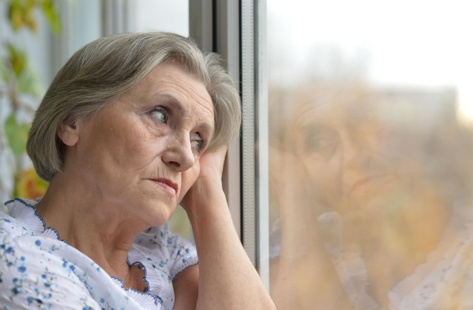 An older adult with depression looks out the window in quiet contemplation.