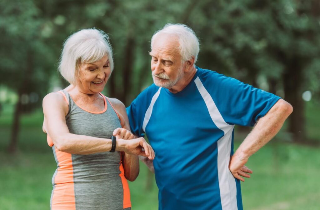 An older adult laughs outside while showing their jogging partner the features of their wearable smart watch